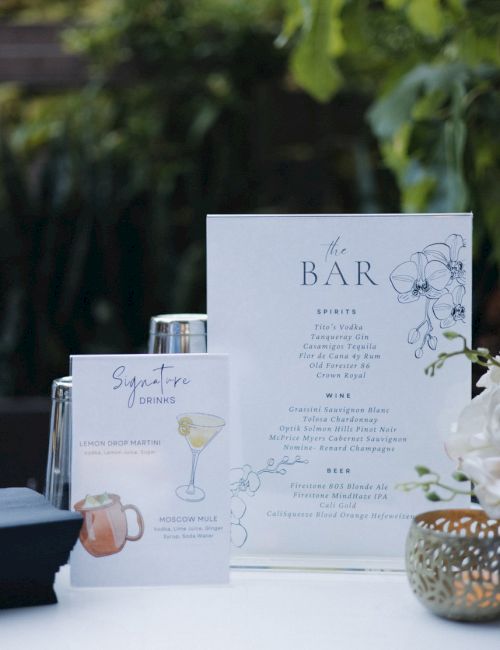 The image shows a bar menu setup with a list of spirits, wine, beer, and signature drinks, set outdoors with a floral decor accent.
