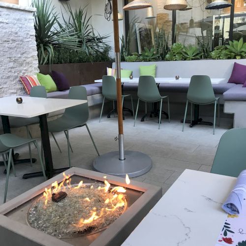An outdoor patio with a fire pit, tables, chairs, and vibrant cushions creating a cozy atmosphere.