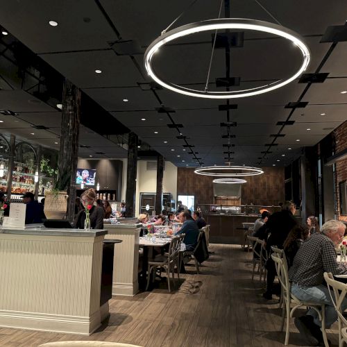 A modern restaurant interior with circular lights, people dining, and a bar area in the background.