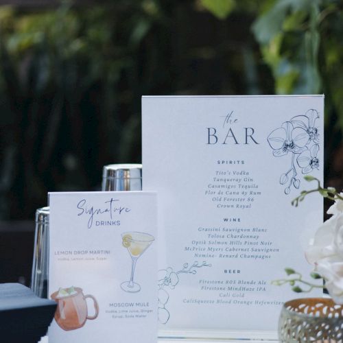 The image shows a bar setup with a drink menu, shaker, decorative plant, and signature cocktail list on a table.