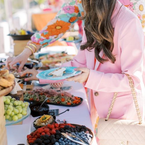 People at a buffet table with various fruits and snacks, including berries and grapes, on display.