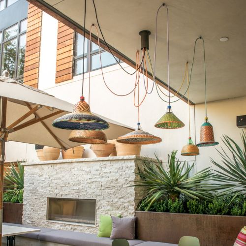 A cozy outdoor seating area features colorful hanging lights, modern furniture, large plants, and a stone fireplace.